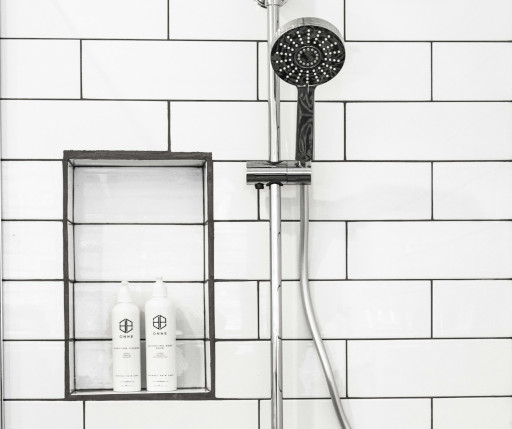 White tile wall with shower head and shampoo