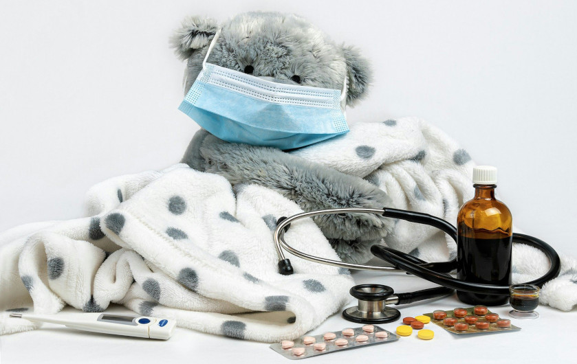 teddy bear with a mask and blankets, depicting illness.